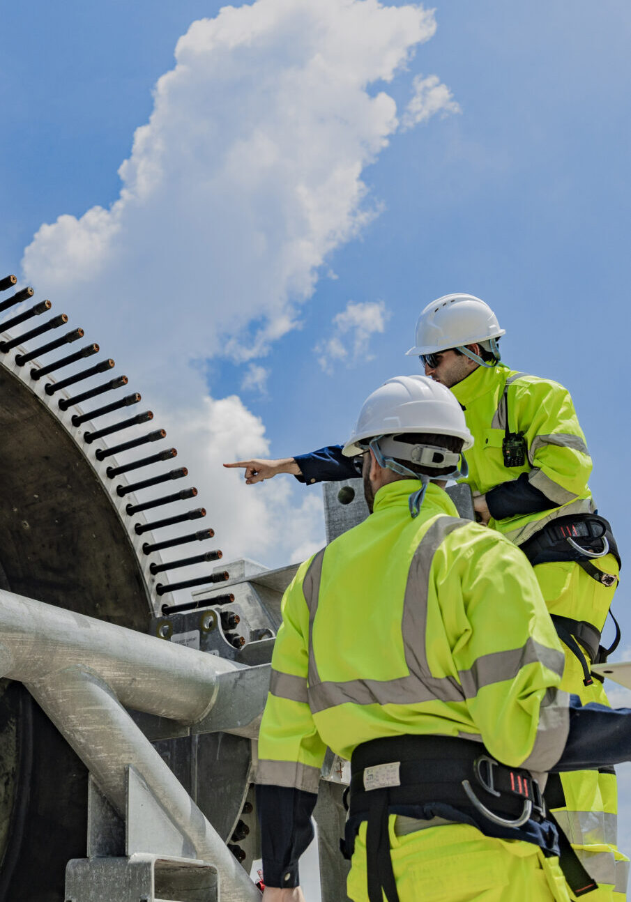 Two engineers work on a wind turbine component, with one using a Two engineers work on a wind turbine component, with one using a laptop and the other inspecting parts on a ladder. renewable energy technology, wind power projects, and teamwork in the energy sector.
