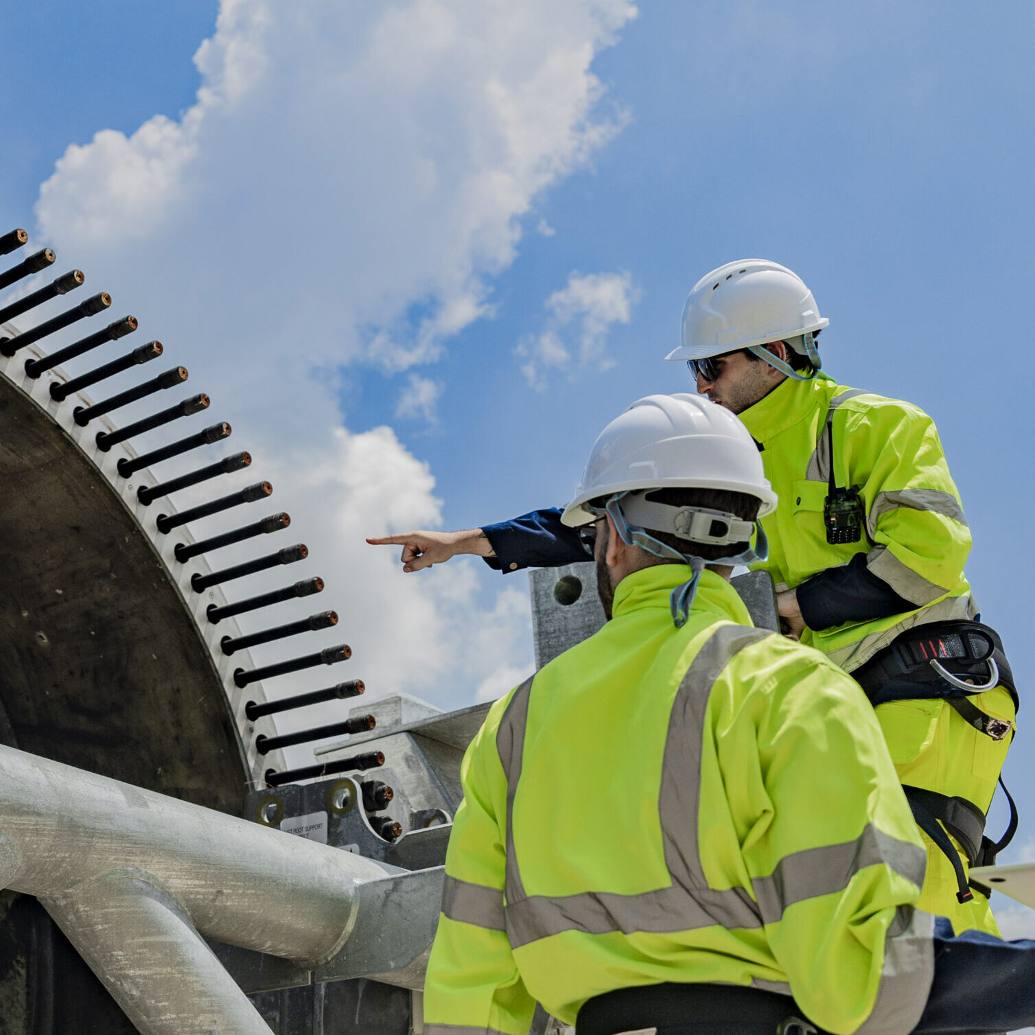Two engineers work on a wind turbine component, with one using a laptop and the other inspecting parts on a ladder. renewable energy technology, wind power projects, and teamwork in the energy sector.