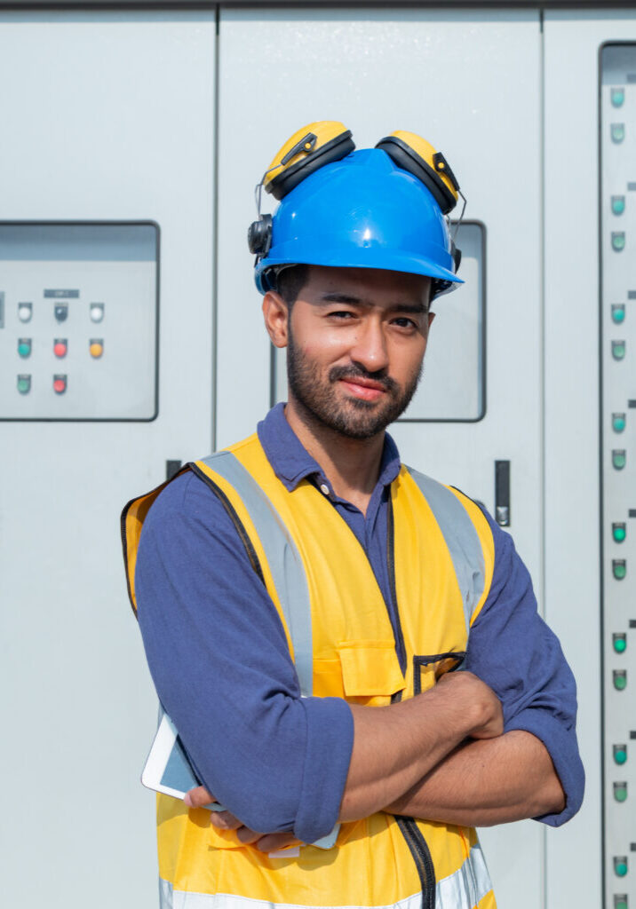 Technician Operating Control Panel in Industrial Setting A technician in high visibility gear operates a control panel while holding a tablet, managing systems at an industrial facility.