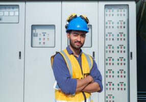 A technician in high visibility gear operates a control panel while holding a tablet, managing systems at an industrial facility.